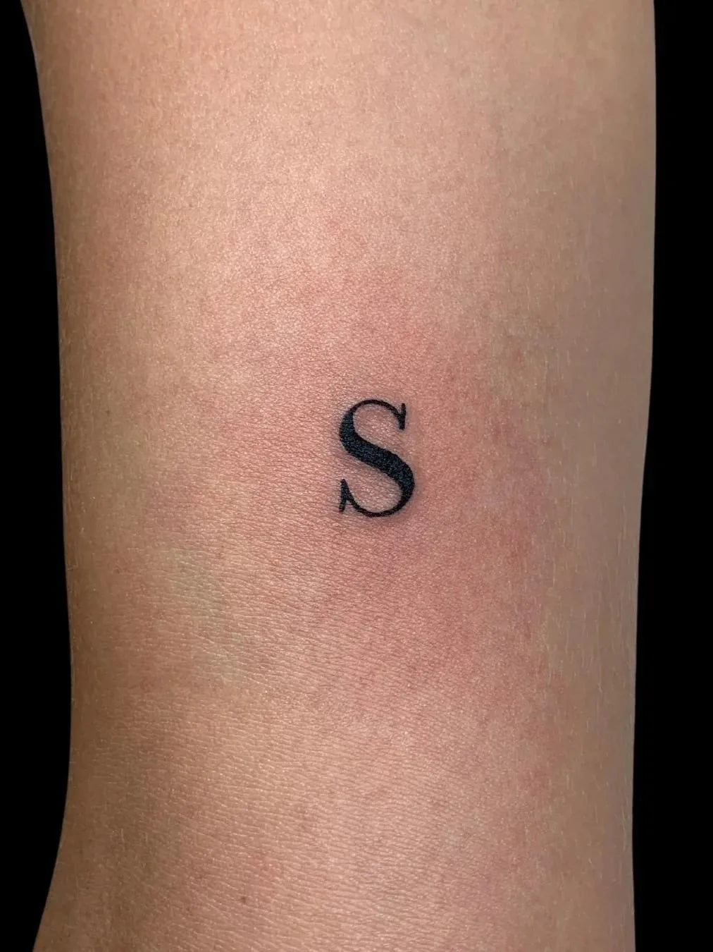 Small minimalist letter 'S' tattoo on a forearm
