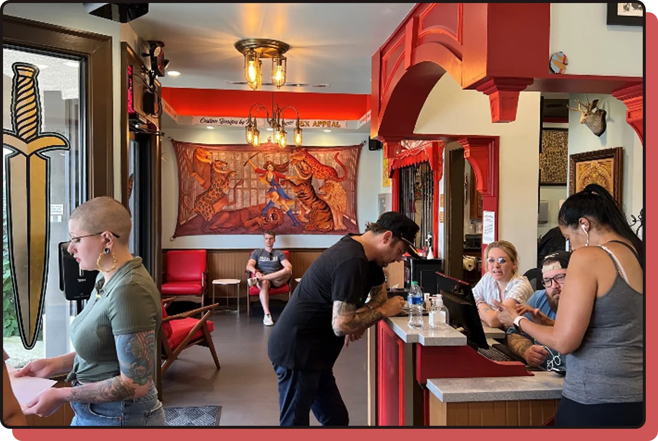 Ink & Dagger Tattoo studio lobby and front desk, with staff and clients beneath vintage red decor and dagger signage