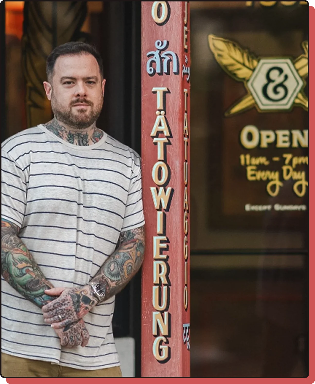 Tattooed man standing outside the Ink & Dagger Tattoo storefront next to the shop sign and open hours
